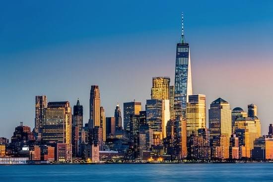 The Lower Manhattan skyline at dusk, One World Trade Center lit above the harbor
