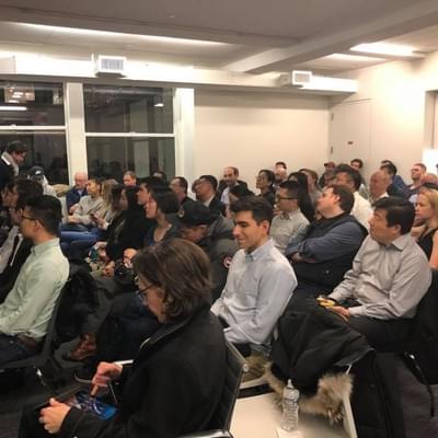 A packed room of attendees smiling toward the stage during a Harvard Alumni in Tech talk
