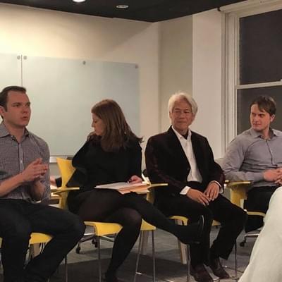 Four panelists seated in a semicircle, one gesturing as he speaks, during a panel discussion