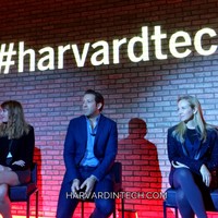 Panelists seated on stage in front of a large illuminated #harvardtech sign