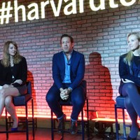 Three panelists seated on stage beneath a lit #harvardtech sign