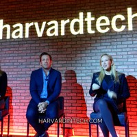 Panelists on stage beneath a large illuminated #harvardtech sign at an evening event