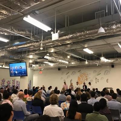 A panel underway on a low stage in a large open office, with a full audience seated in rows