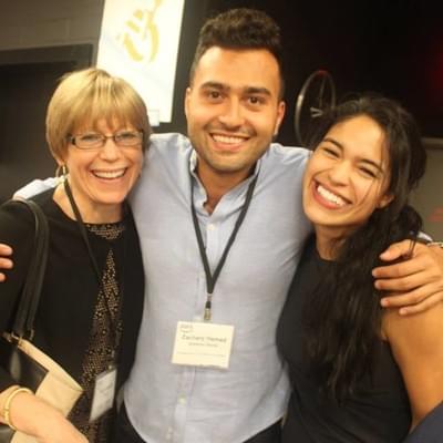 Three attendees wearing conference badges posing together and smiling at an event