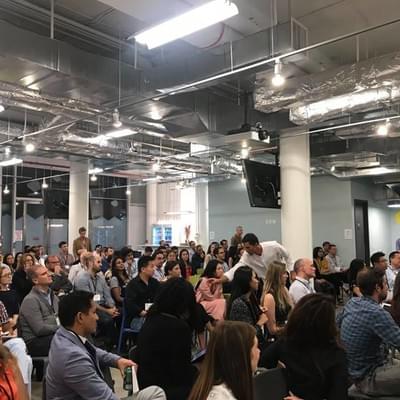 A large audience seated in an open-plan office space watching a presentation