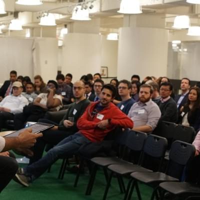 Attendees seated in rows of chairs listening, one leaning back and smiling