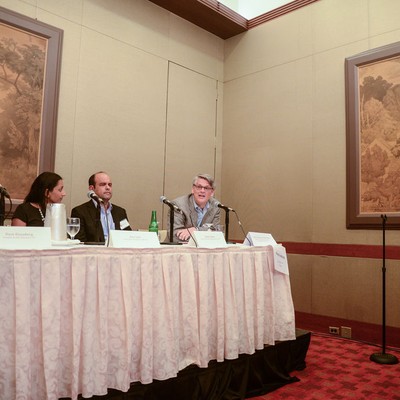 Three speakers seated behind a draped table with microphones and name cards