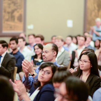 Audience members applauding during a talk in a wood-panelled hall