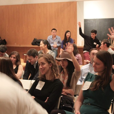Attendees seated in a lecture hall, several raising their hands to ask questions