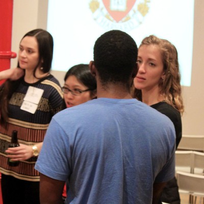 Attendees talking in front of a projected Harvard crest at a reception