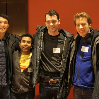 Four attendees in winter coats posing together at an event