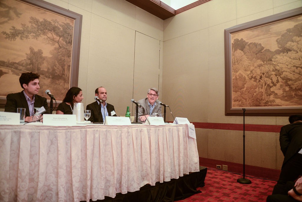 Four panelists seated behind a draped table with microphones during a Harvard Alumni in Tech panel